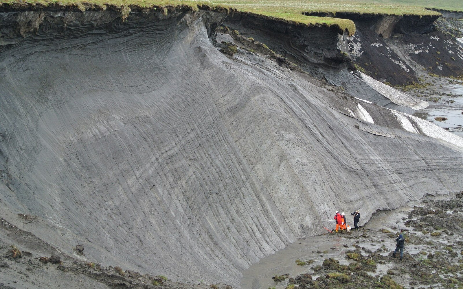 Researchers stand at the base of a large permafrost thaw slump exposing layered frozen ground